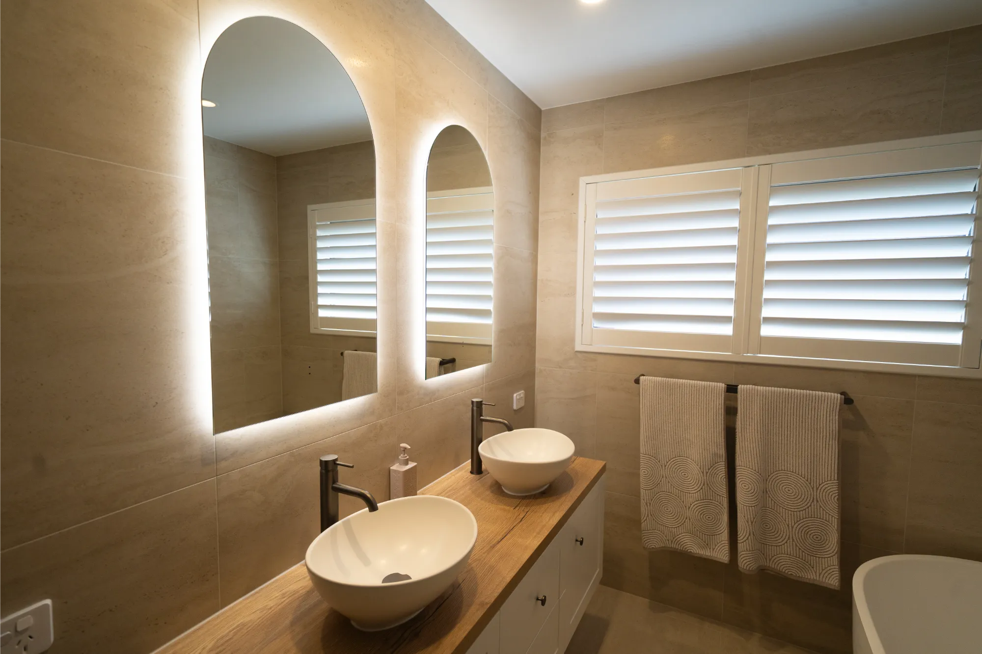 Double vanity with timber benchtop and arched backlit mirrors